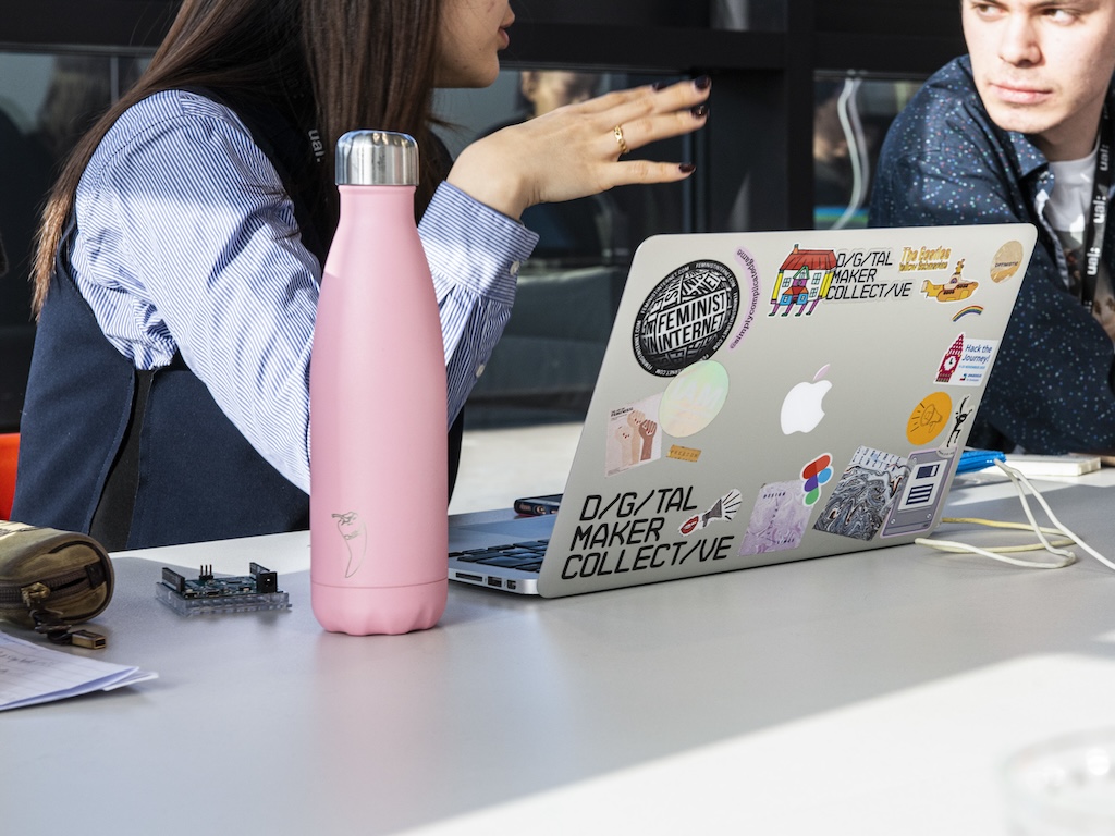 Two students are conversing in a computing workshop area with laptops in front of them